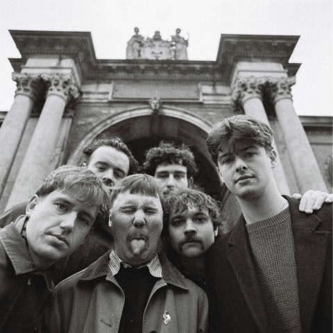 The band in black and white under a stone archway, one of them sticking his tongue out