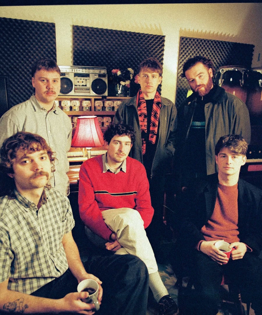 The six members of Fizzy Orange in their home studio, with a boombox and a red lamp behind them